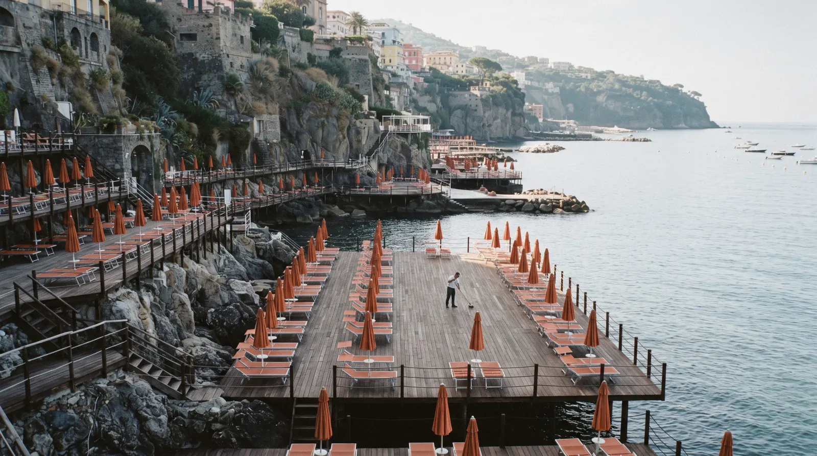 Wooden bathing platforms over clear green water below the Sorrento cliffs with swimmers beyond the ladders