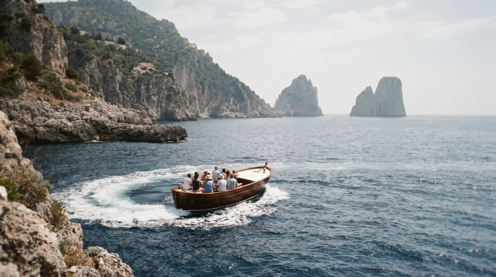 Wooden gozzo boat cutting across green water off the Sorrento coast in the morning, cliffs and Villa Comunale gardens above